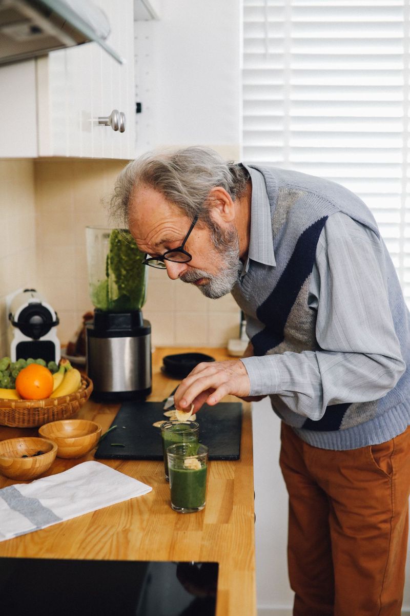 Starszy mężczyzna przygotowujący zielone smoothie w kuchni