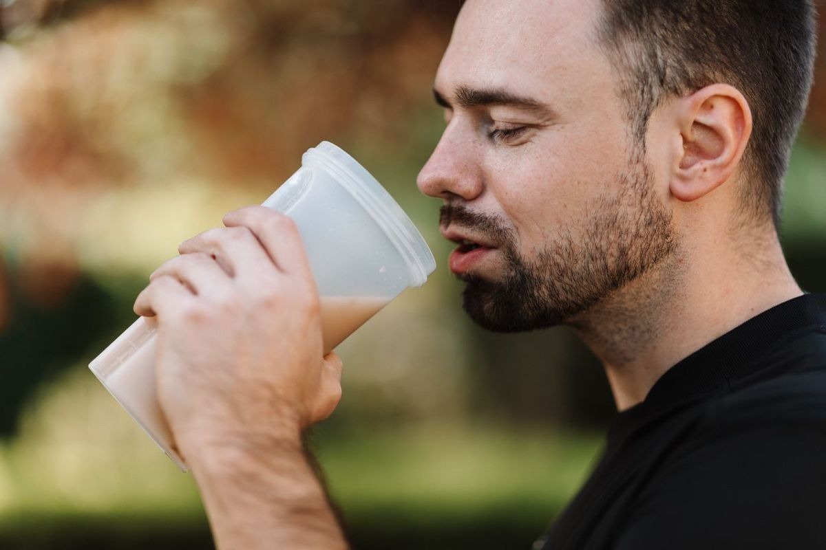 Brodaty mężczyzna pijący smoothie z kubka na świeżym powietrzu
