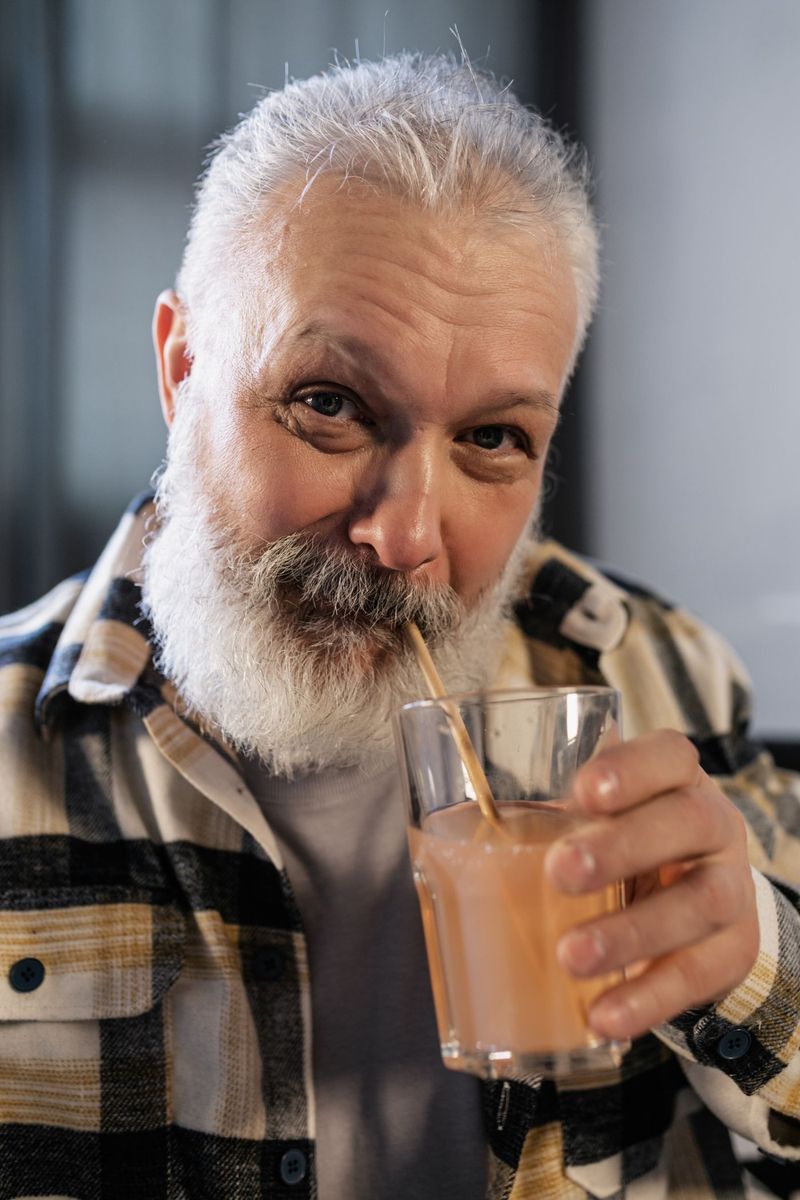 Starszy mężczyzna z siwą brodą pijący smoothie przez słomkę